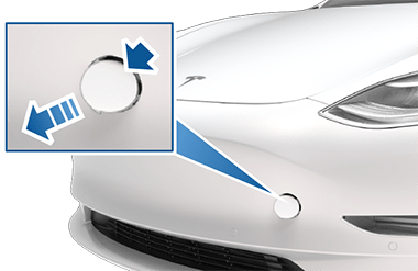Dianteira do veículo com uma caixa de zoom e setas a indicar que deve pressionar o canto superior direito da tampa do olhal de reboque para a soltar.