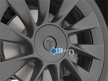 Šipka směřující od nástroje na matice kol ke kruhové prohlubni pod základnou loga Tesla „T“ na krytu matice kol